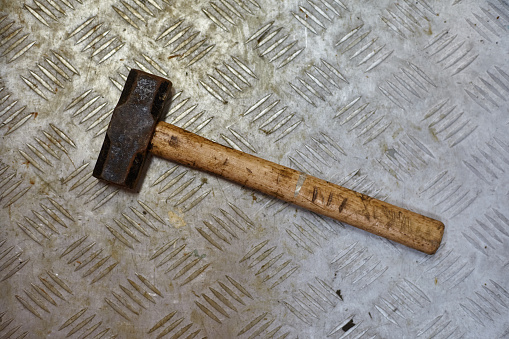 Dirty and rusty metal sledgehammer with wooden handle on metal work table.