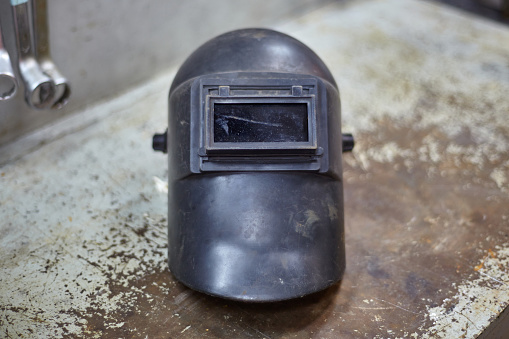 Black welding helmet on metal table in workshop, close up.
