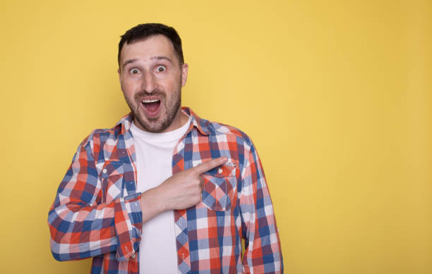 istock Happy handsome man point finger look aside posing isolated on yellow studio background. Copy space Banner Mockup. People emotions. Lifestyle concept. 1691870101