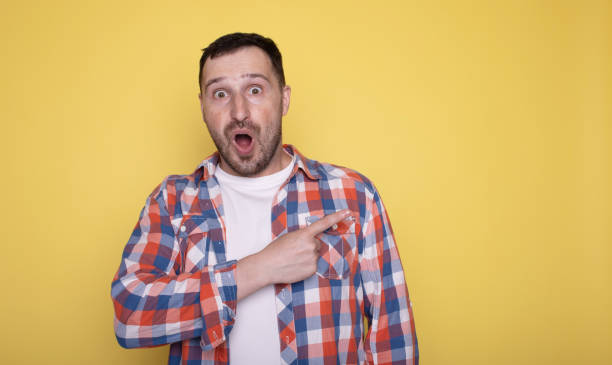 istock Happy handsome man point finger look aside posing isolated on yellow studio background. Copy space Banner Mockup. People emotions. Lifestyle concept. 1691870102