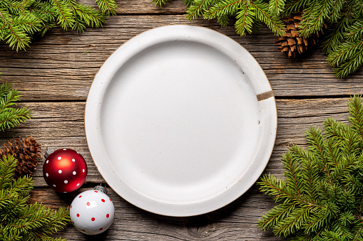 Table setting from above with empty plate, Christmas Fir tree branches and pine cones on wooden background. Flat lay