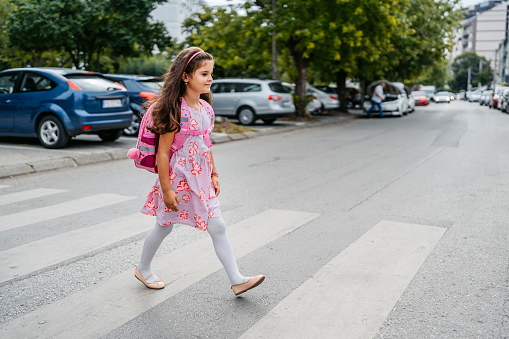 Little girl with a backpack crossing the street while heading to school alone.
