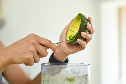 Woman putting sliced avocado into blender for making healthy smoothie. Dieting and healthy lifestyle concept.
