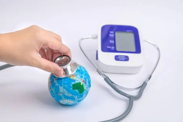 Close up man's hand used stethoscope for health check the globe earth beside digital blood-pressure meter. World environment and earth day concept. save the world concept.