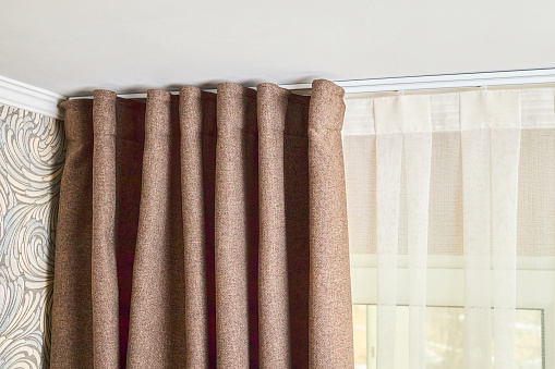 Ceiling cornice with drapes white curtain or tulle. Interior details close up. White ceiling plastic ceiling cornice with two rails brown matting fabric curtains and transparent curtains near window