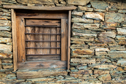 Traditional stone hut in Uttarakhand, India, featuring a wooden window set within a rugged stone wall, showcasing local countryside architecture
