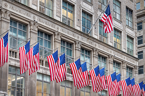 Fifth Avenue, Manhattan, New York, USA - August 8th 2023:   Row of American flags on the facade of an expensive shop in the center of the business district