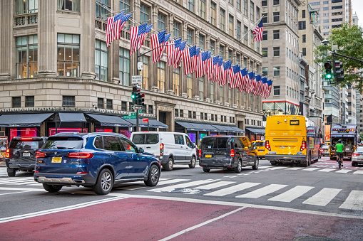 Fifth Avenue, Manhattan, New York, USA - August 8th 2023:   Row of American flags on the facade of an expensive shop in the center of the business district with traffic in front