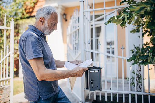 One man, senior male reading his mail while standing in front of his house outdoors.