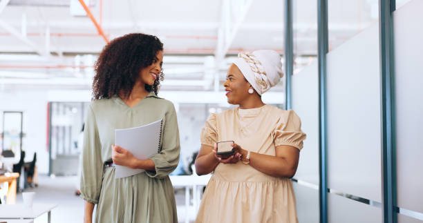 istock Business team, talking and walking together for communication, gossip or happy conversation while working at a coworking office. Black women with a phone and paperwork while sharing ideas and advice 1691948391