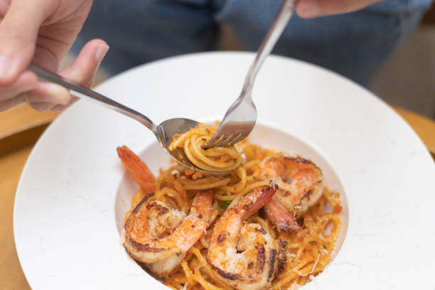istock Woman using fork to roll spaghetti on white plate, A woman eat Kee Mao Shrimp Spaghetti with feeling happy and enjoy to eat food in the restaurant. Enjoy eating, refreshing drinks, Taste concept. 1691948961