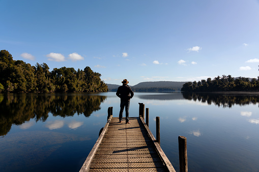 Sporting an Indiana Jones-style hat, a man in his fifties takes in the wonders of Lake Mapourika, on the West Coast of New Zealand's South Island.