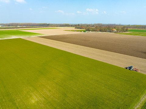 Tractor preparing the soil for planting crops during a sunny and dry springtime day. Aerial view drone view from directly above.