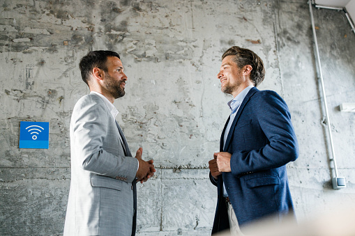 Smiling male entrepreneurs communicating by the wall in the office. Copy space.