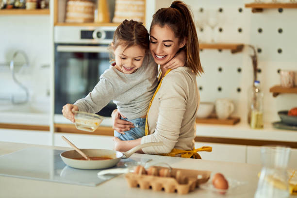 istock A smiling mother holding his daughter while shes putting eggs into the pan. 1691989715