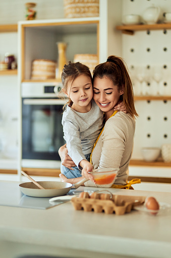 Smiling mother holding her daughter, helping each other making breakfast.