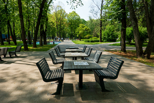 Color image depicting chairs and tables arranged at an outdoors cafe in central London, UK. It is a beautiful green space lined with trees and illuminated with fairy lights. There are bowls of sugar on the tables, but there are no people around. Room for copy space.