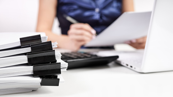 A stack of papers with Binder Clips against the background of an office worker working with documents