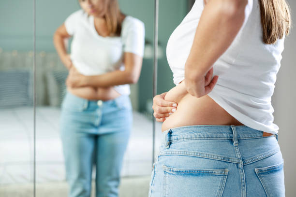 istock Young woman touching her belly looking in mirror at home 1691997512