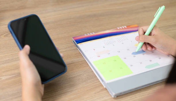 istock Woman holding mobile phone for checking appointments on mobile phone with taking notes on calendar. Take notes for Debt payment plan. Event planner timetable agenda plan, Calendar event plan. 1691999841