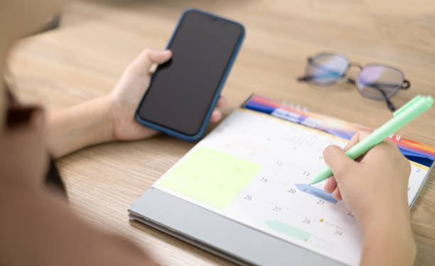 istock A woman checking planner on mobile phone with taking notes on calendar. Take notes for meeting appointments or Debt payment. Event planner timetable agenda plan. Calendar event plan, work planning 1691999862