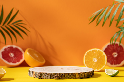 Empty wooden round podium on colorful yellow and orange background surrounded by citrus fruits