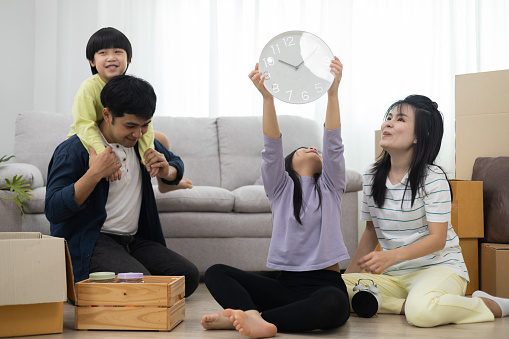 Asian family smiles and laughs happily in new home. Adorable sons and daughters play with boxes while moving house. family day activities together. Family photo or communication concept.