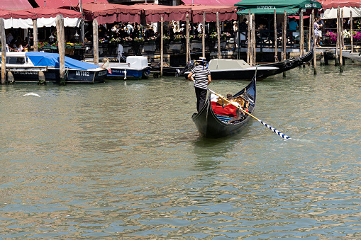 Venice, Veneto, Italy- June 26, 2023; On the grand canal of Venice-Italy, a couple of tourists take a ride on a gondola, typical maritime transport of Venice, the boat is steered by a man.