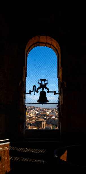 トレ・デ・ラ・クレレシアの復元されたブロンズの鐘の逆光のシルエットと、アーチ型の窓から夕方の日差しが差し込み、サラマンカの街を見下ろす - church bell tower temple catholicism ストックフォトと画像