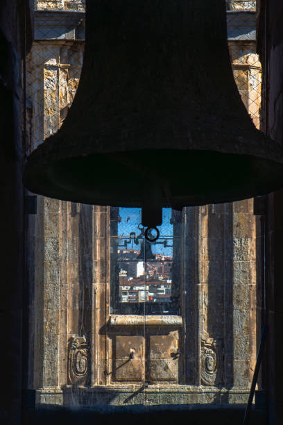 クレレシア教会の塔から復元された2つのブロンズの鐘のバックライト付きシルエットで、保護用の鳩防止メッシュを備えたアーチ型の窓からサラマンカの街を眺めることができます。 - church bell tower temple catholicism ストックフォトと画像