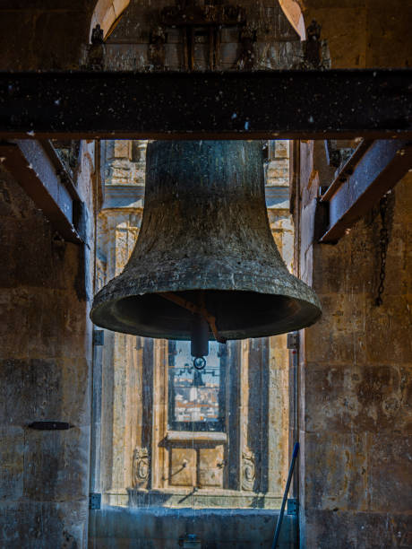 復元されたブロンズの鐘ですが、サラマンカのクレレシア教会の鐘楼からの鳩の糞があり、鉄の梁と高い景色を背景にした街で保護されています。 - church bell tower temple catholicism ストックフォトと画像