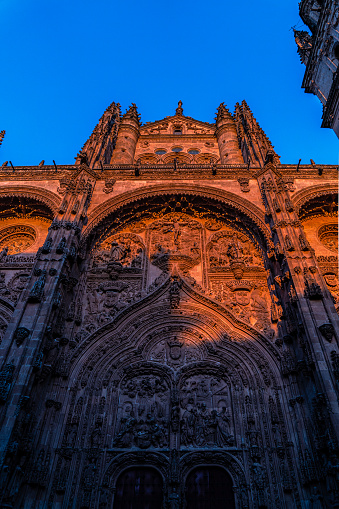 The front of the new cathedral of Salamanca with bas-reliefs of religious motifs, from a low angle view, illuminated by the golden orange light of sunset with shadows cast from the opposite building.