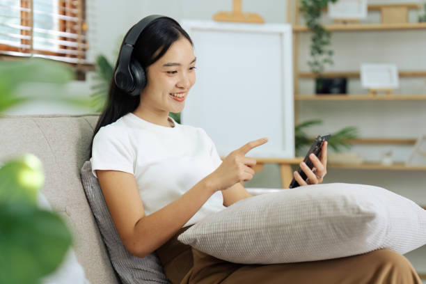 молодая женщина отдыхает и слушает музыку по телефону на диване - room service audio стоковые фото и изображения