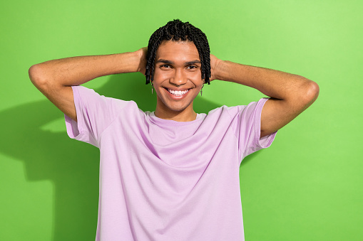 Photo of nice positive person toothy smile hands behind head enjoy free time isolated on green color background.