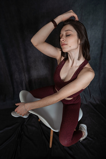 young slim woman in red sport cloth bra posign near chair isolated on black. lifestyle