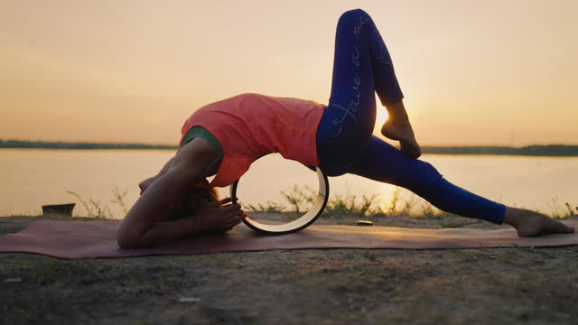 Athletic Woman Doing Asana On Stretching Yoga Circle In Nature, View On Sunset Over River