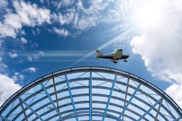 Small private propeller airplane in motion above a modern airport, against a beautiful clear blue sky with cumulus clouds and sunbeams.