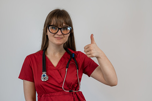 Young woman general practitioner or doctor in red uniform and stethoscope isolated on gray. healthcare worker