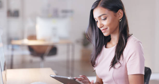 istock Young happy woman with a digital tablet while relaxing in an office at work. One smiling female student taking pictures to post on social media while sitting alone in a library 1692083775