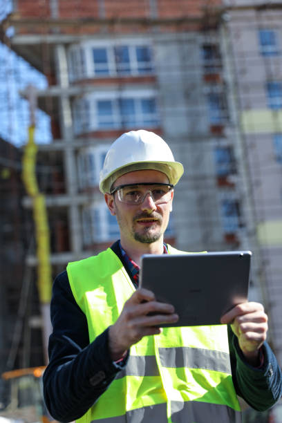istock Male architect using digital tablet at construction site, he wears a protective vest and helmet 1692086118
