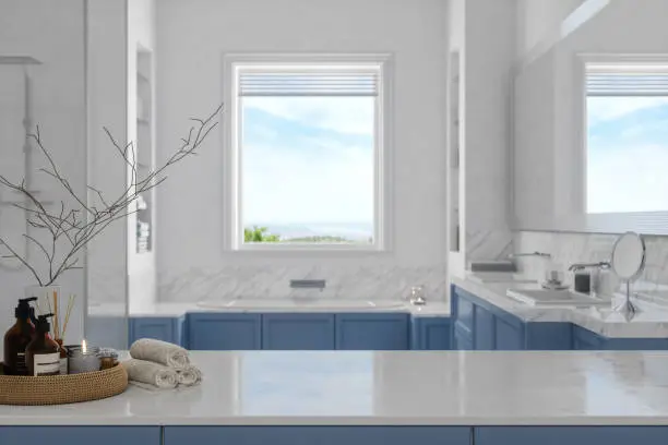White marble countertop in a calming bathroom featuring a blue cabinet, city-view window, and various amenities like towels and soap.