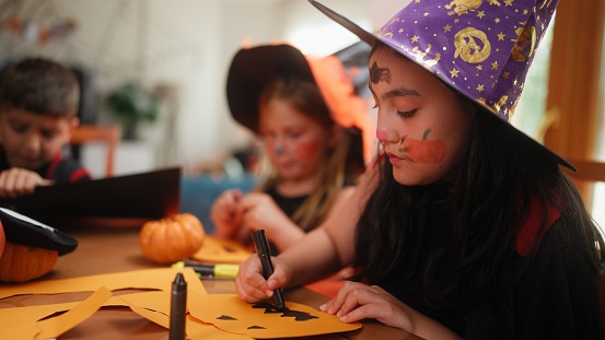A group of small children friends are making Halloween decorations during a house Halloween party gathering.