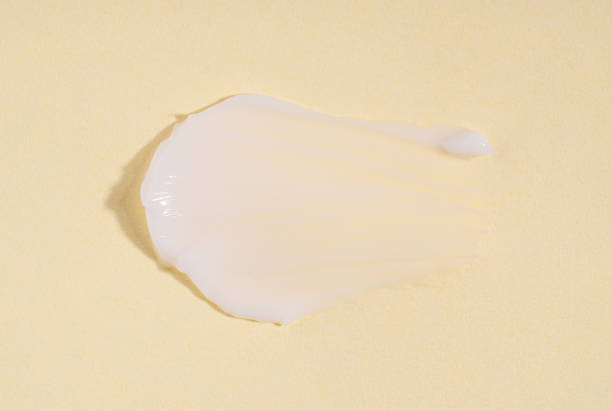 黄色の背景に白いクリームのテクスチャー。テクスチャー加工されたホワイトクリームの汚れ見本。パステルイエローの背景にクリーミーなテクスチャーの化粧品塗抹標本