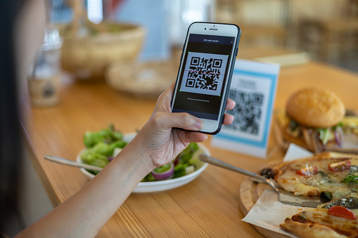 Customer scanning tag in coffee shop to pay online. Close up of hand scanning QR code for cashless payment at cafeteria. Girl framing QR code to make a purchase, small business accepts digital payment