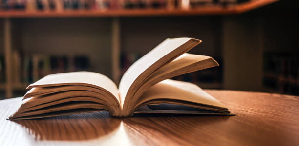 istock Vintage style.An open book or textbook vintage style in the library with light from the window on the reading table and the corridor of the bookshelves in the school classroom background.Education learning concept 1692115429