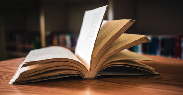 istock Vintage style.An open book or textbook vintage style in the library with light from the window on the reading table and the corridor of the bookshelves in the school classroom background.Education learning concept 1692115437