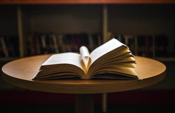 Vintage style.An open book or textbook vintage style in the library with light from the window on the reading table and the corridor of the bookshelves in the school classroom background.Education learning concept