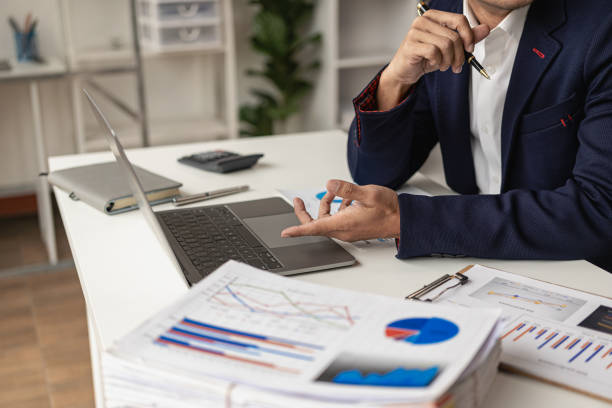 istock Asian accountant working with documents and accounting using laptop A male businessman is calculating and analyzing company revenue sitting at a table inside an office building. 1692118983
