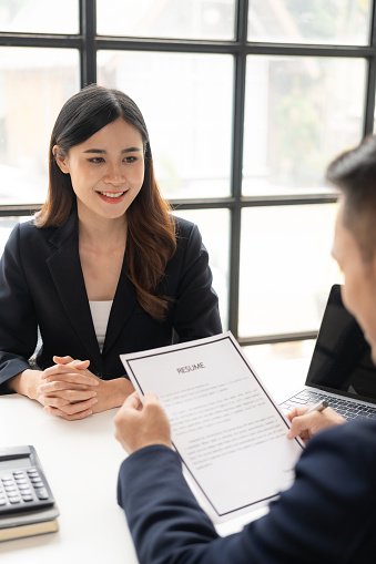 Young Asian woman is interviewing for a job in the office. Focus on tips for writing a resume Employers are checking good CVs of applicants with prepared skills. Brokers are considering