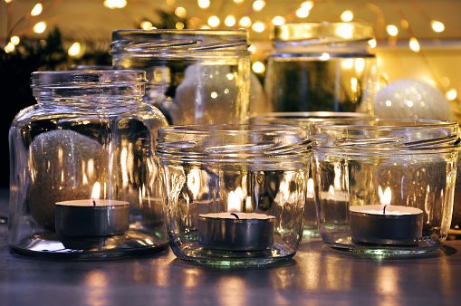 Close-up of burning candles in glass jars and Christmas lights in background. For holiday and lifestyle greeting card or background - Holiday, Christmas and new year concept